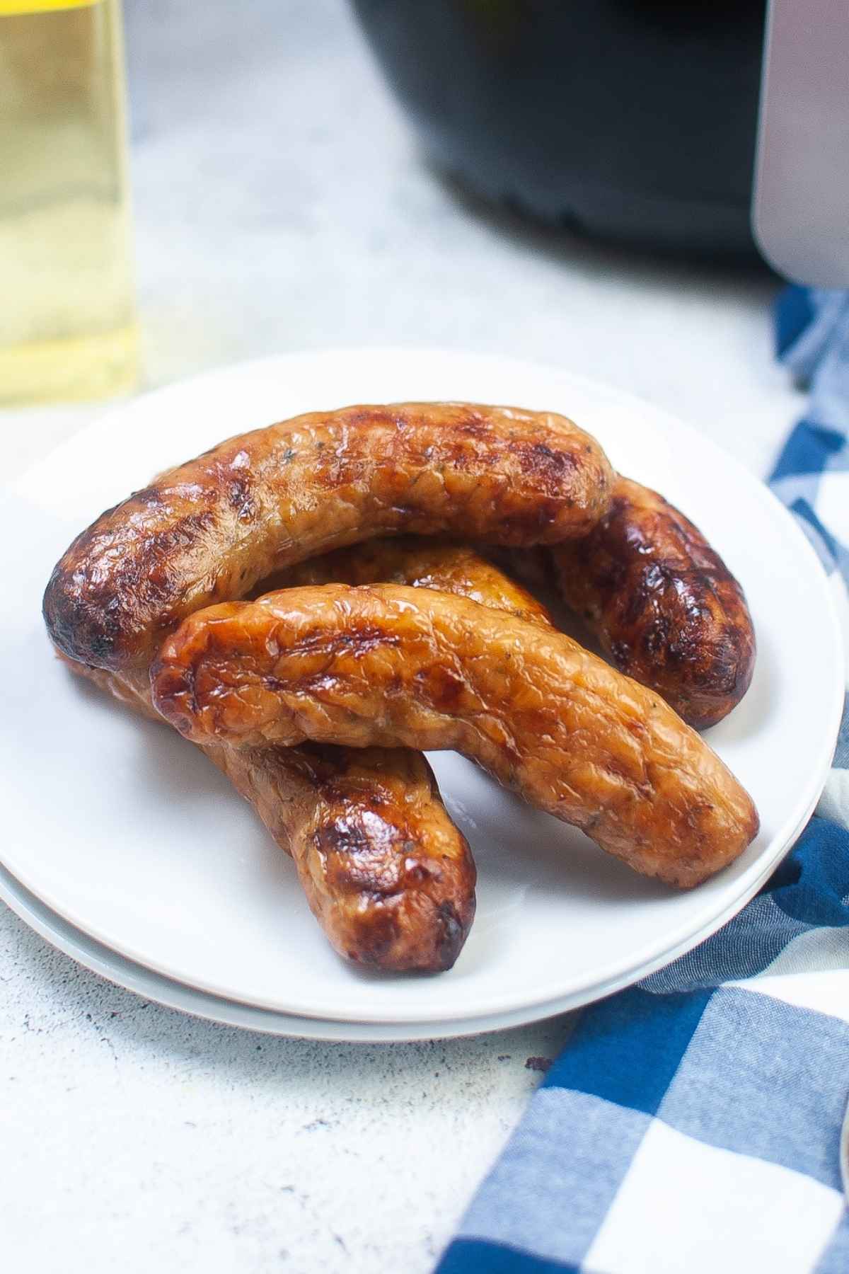 Side view of juicy air fryer sausage links stacked on a white plate, highlighting their browned, crispy exterior.