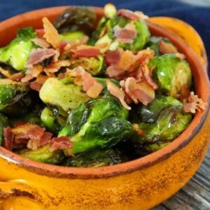 Crispy air fryer brussels sprouts in an orange bowl topped with bacon pieces and tossed in a browned balsamic butter.