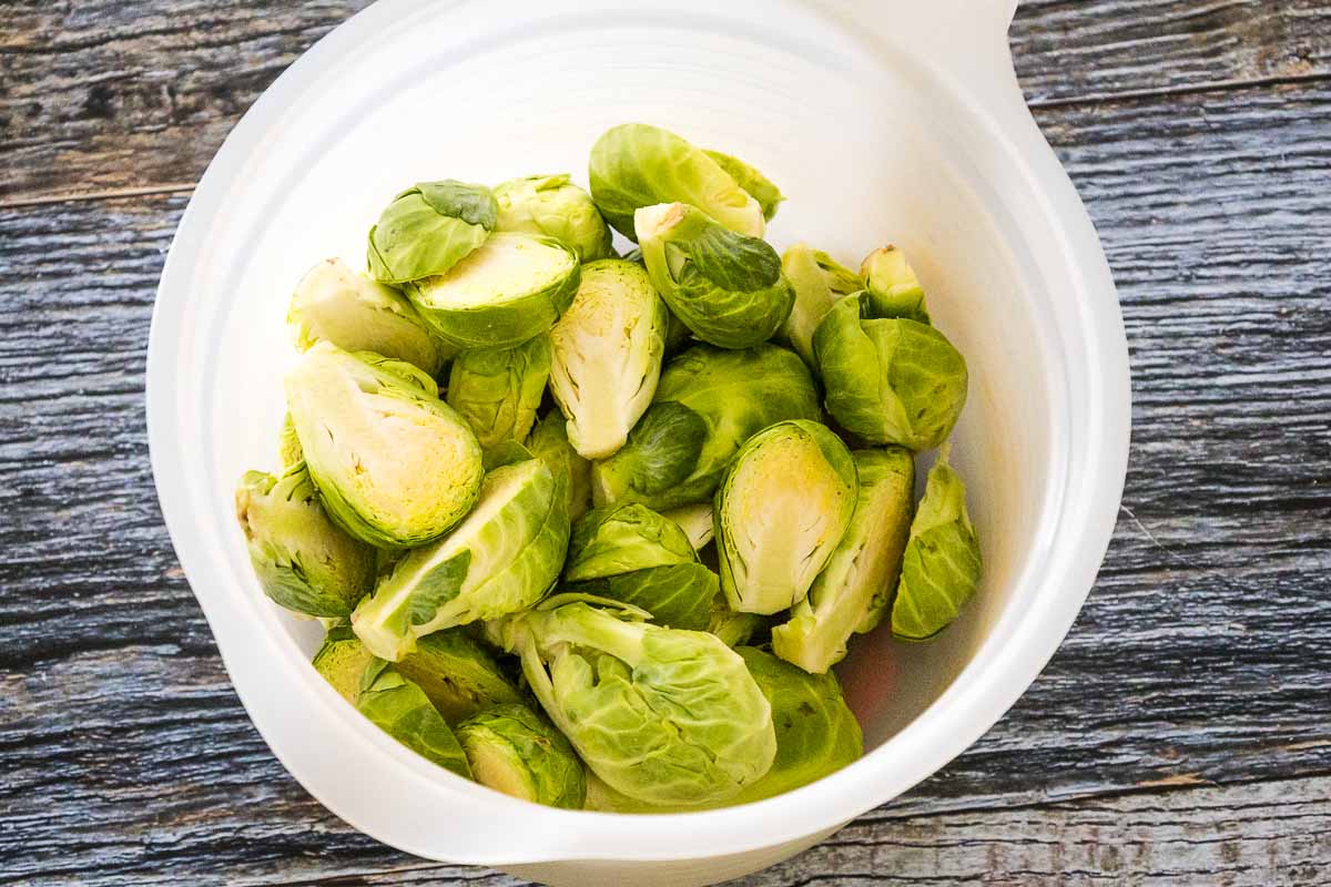 Raw brussels sprouts cut in half and in a white mixing bowl.