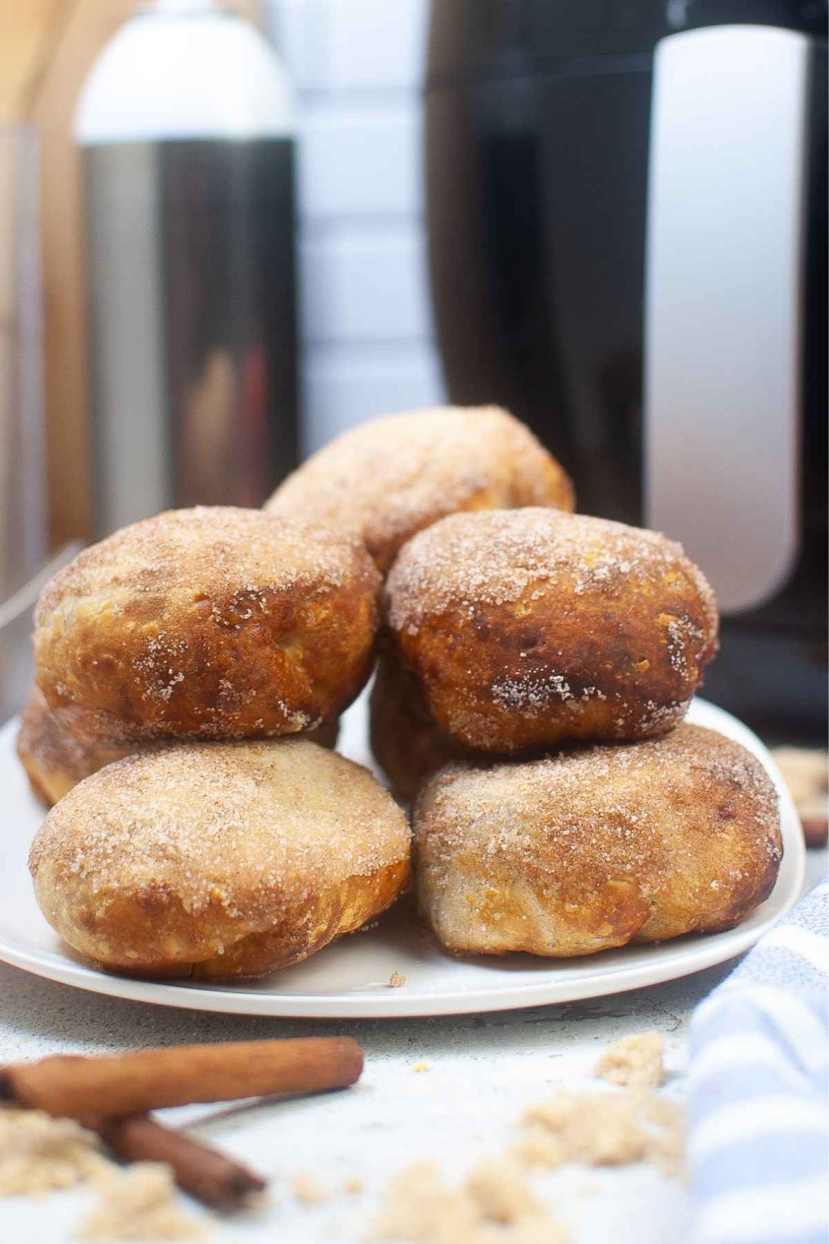 plate stacked with golden brown pumpkin pie bombs coated in cinnamon sugar, with an air fryer in the background
