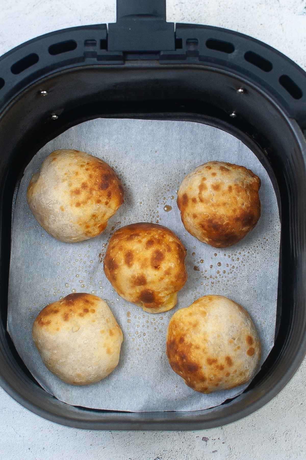 Air fried pumpkin pie bombs resting on parchment inside an air fryer basket, showing golden, slightly crispy tops.