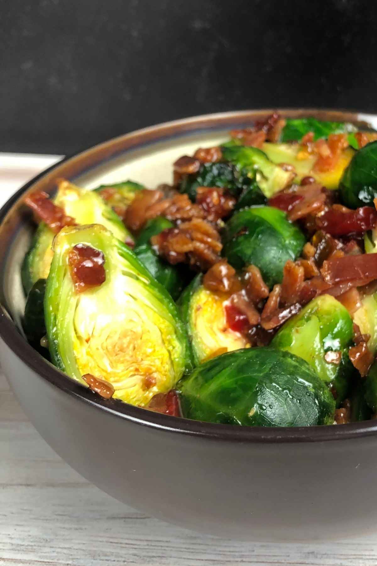 A brown and cream serving bowl filled with crispy air-fried pepper jelly Brussel sprouts topped with crumbled bacon.