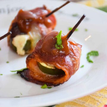 Bacon wrapped venison bites topped with barbecue sauce on a white plate.
