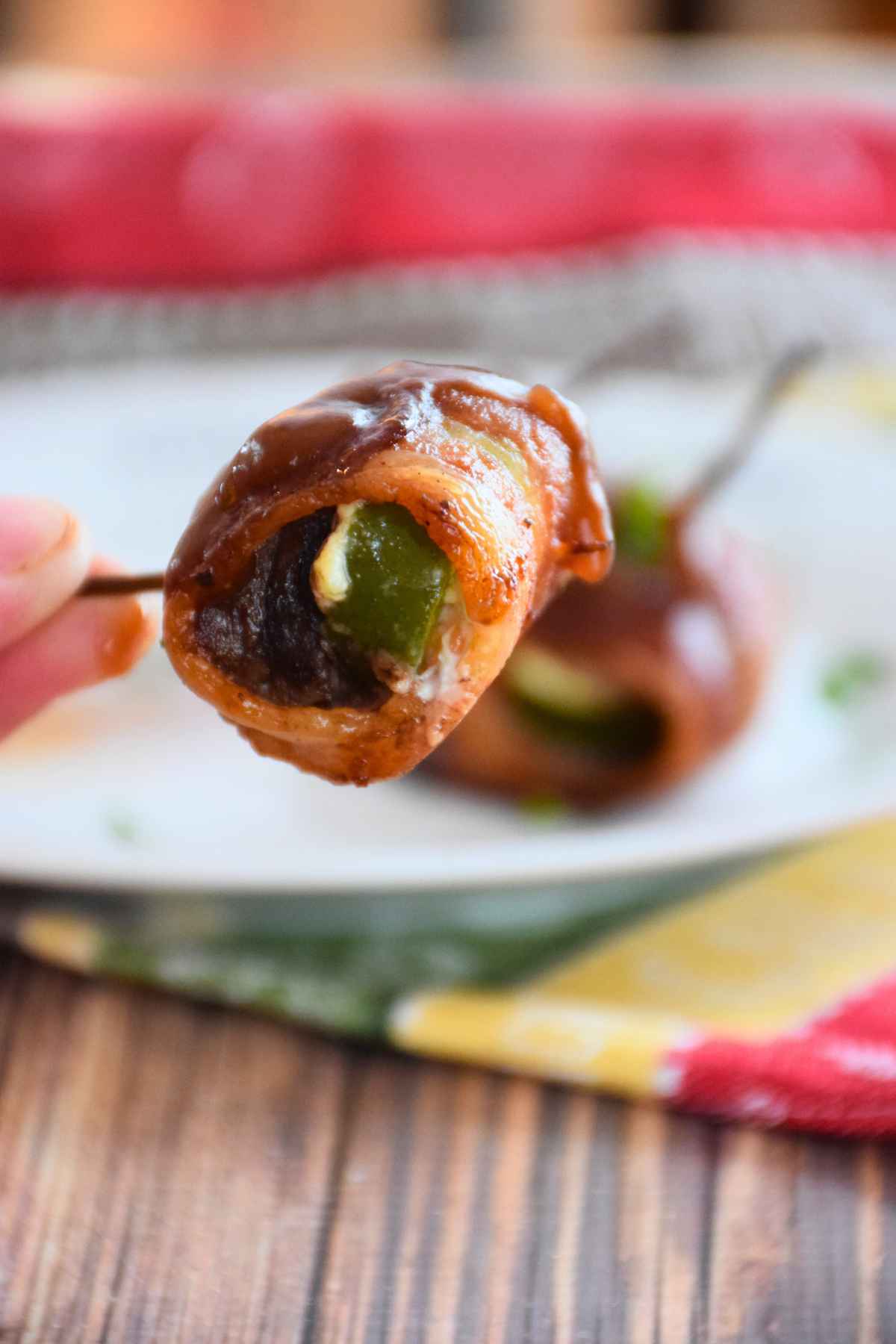 Hand holding a bacon wrapped venison bite with jalapeno and cream cheese.