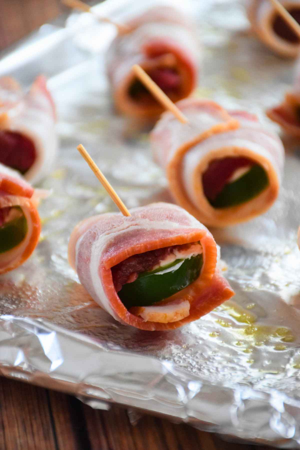 Unbaked bacon wrapped venison appetizer with toothpicks on a foil lined pan.