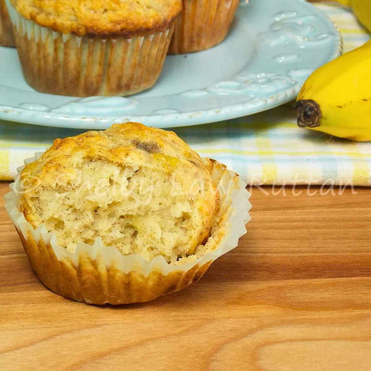 One browned butter banana muffin with the wrapper pulled away and a bite taken out of the muffin.