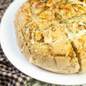 Upclose image of homemade cheesy pull apart bread topped with melted cheese, herbs, and garlic served on a white plate.
