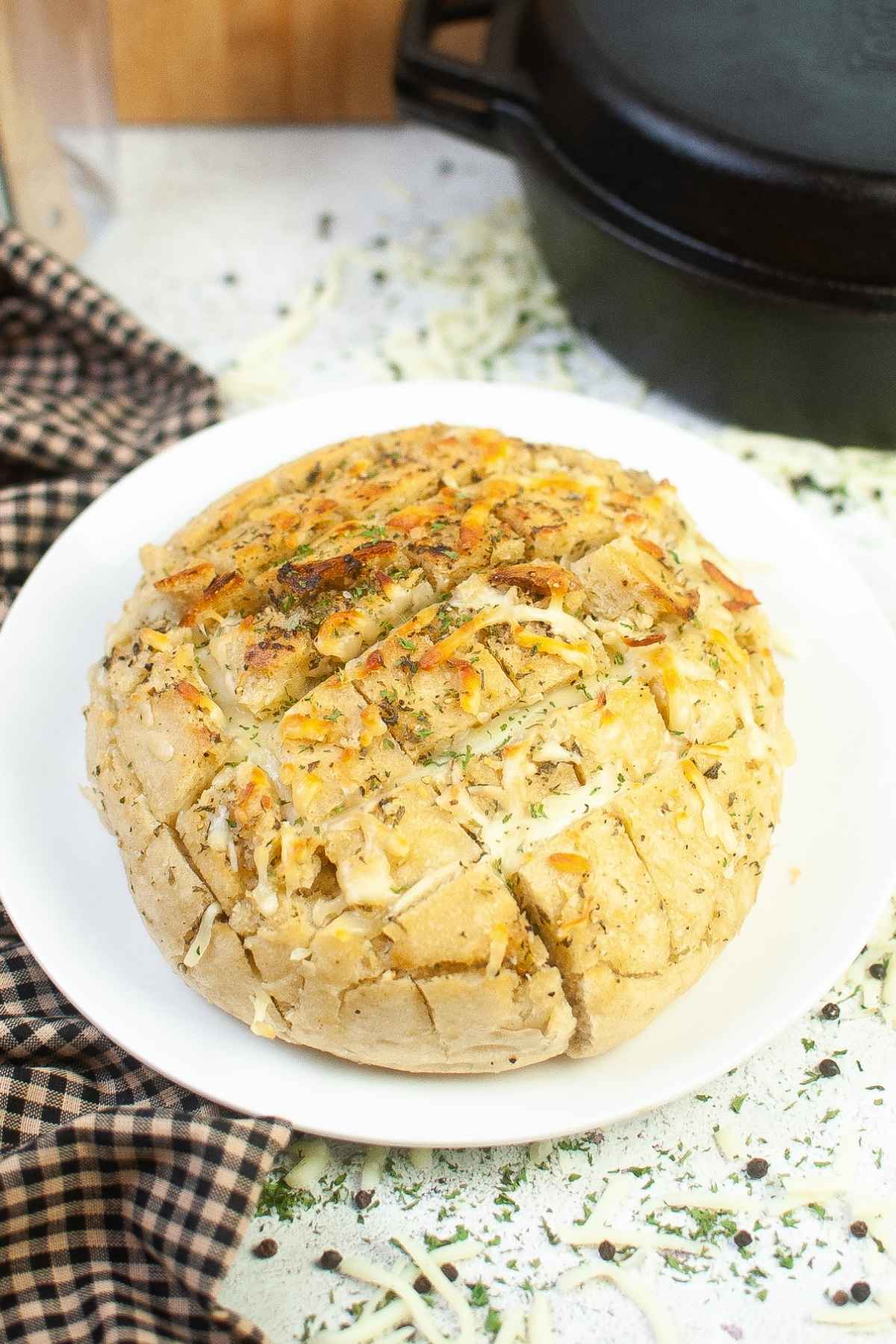 Homemade cheesy pull apart bread topped with melted cheese, herbs, and garlic served on a white plate.