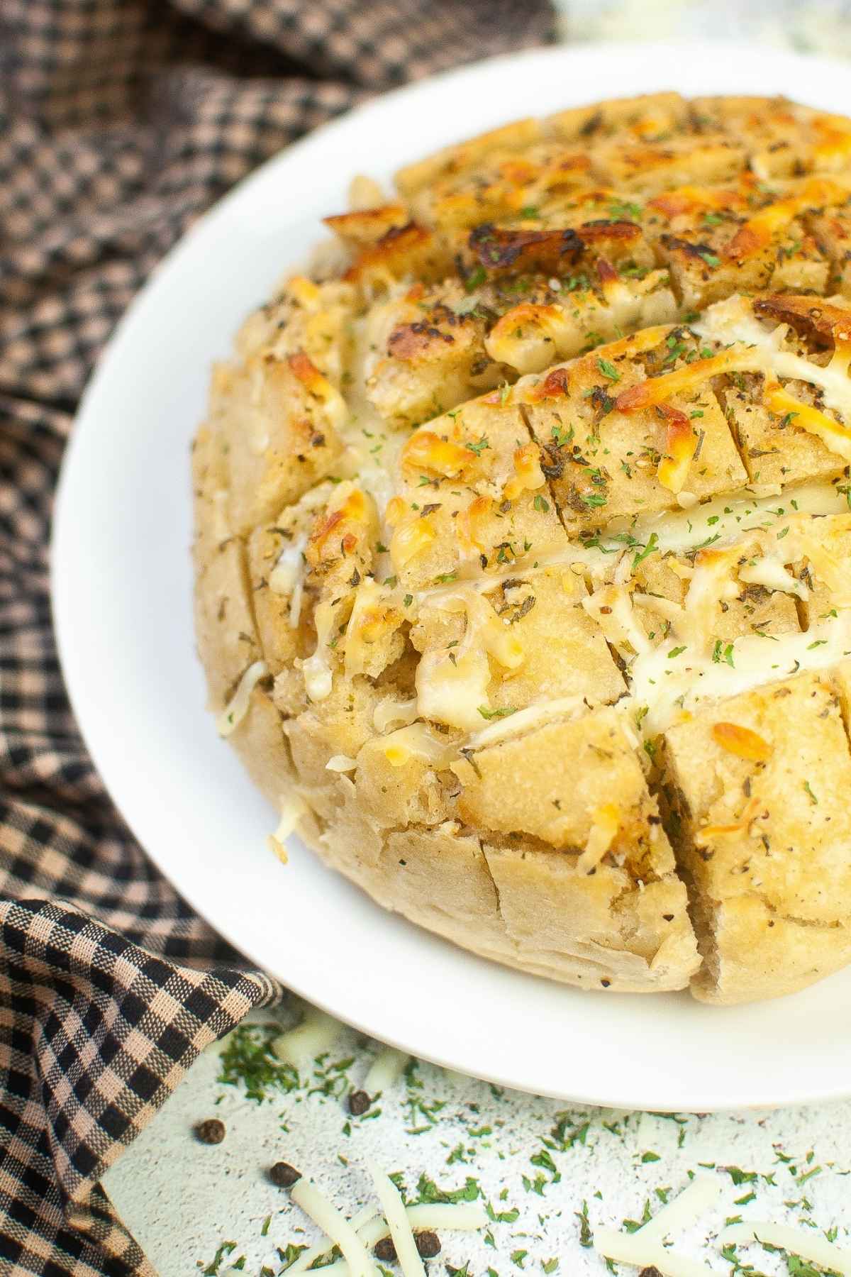 Upclose image of cheesy pull apart bread topped with melted cheese, herbs, and garlic served on a white plate.