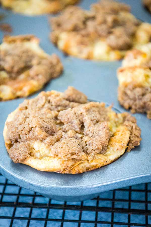 Baked croissant french toast muffins in a muffin tin topped with a cinnamon crumb mixture.