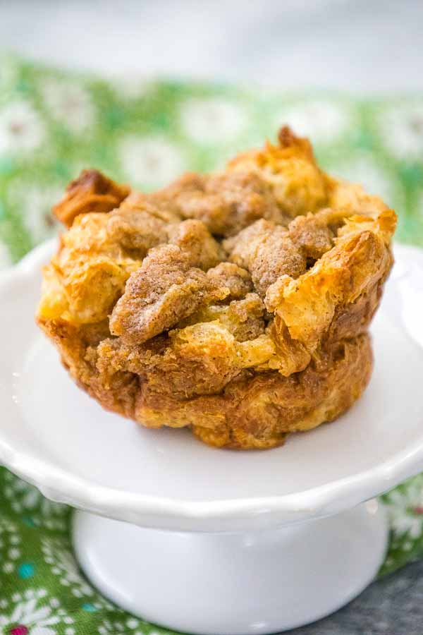 Single croissant French Toast Muffin on a white plate with a green patterned cloth in the background.