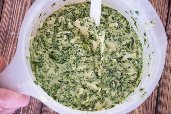 Mixing bowl filled with spinach, egg, and cheese mixture being stirred with a spatula.