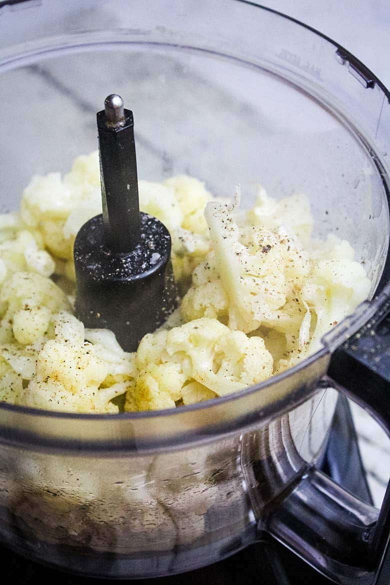 Cooked cauliflower seasoned with pepper inside a food processor, ready to be blended.