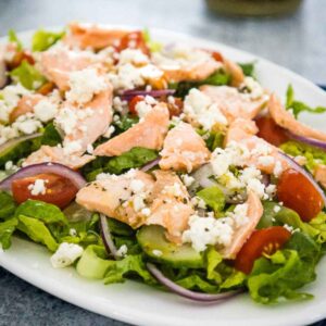 Fresh salmon salad with lettuce, tomatoes, cucumbers, feta cheese, and baked salmon.