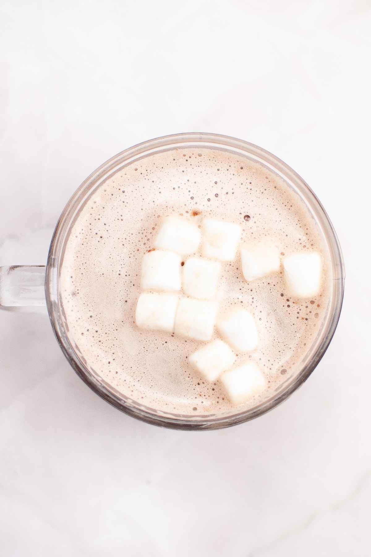 Overhead of a clear glass mug filled with hot chocolate topped with mini marshmallows after a Grinch hot cocoa bomb has melted.