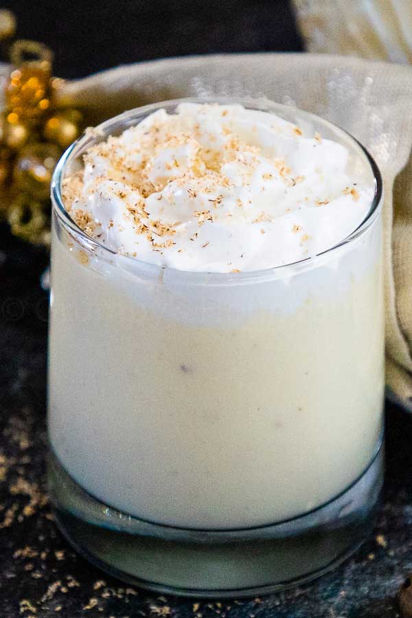 Glass of homemade eggnog topped with whipped cream and a sprinkle of nutmeg.