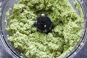 A blended green chickpea and herb mixture inside a food processor.