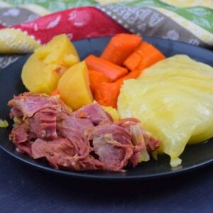 Plated serving of Instant Pot Ham and Cabbage, potatoes, and carrots, on a black dish.