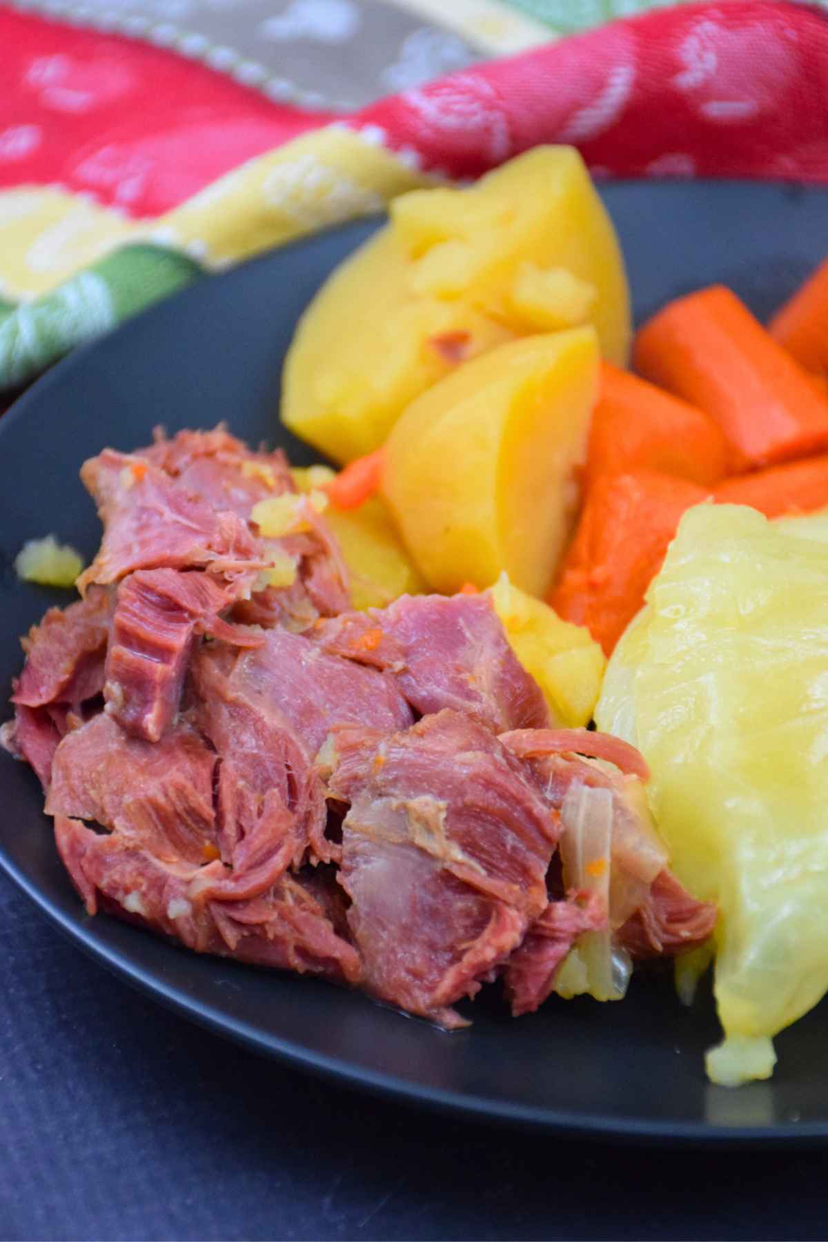 Close up of Instant Pot Ham and Cabbage dinner with potatoes and carrots on a black plate.
