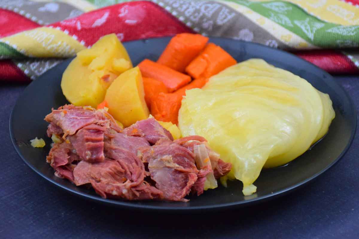 Ham, cabbage, carrots, and potatoes plated together on a black plate with a patterned napkin.