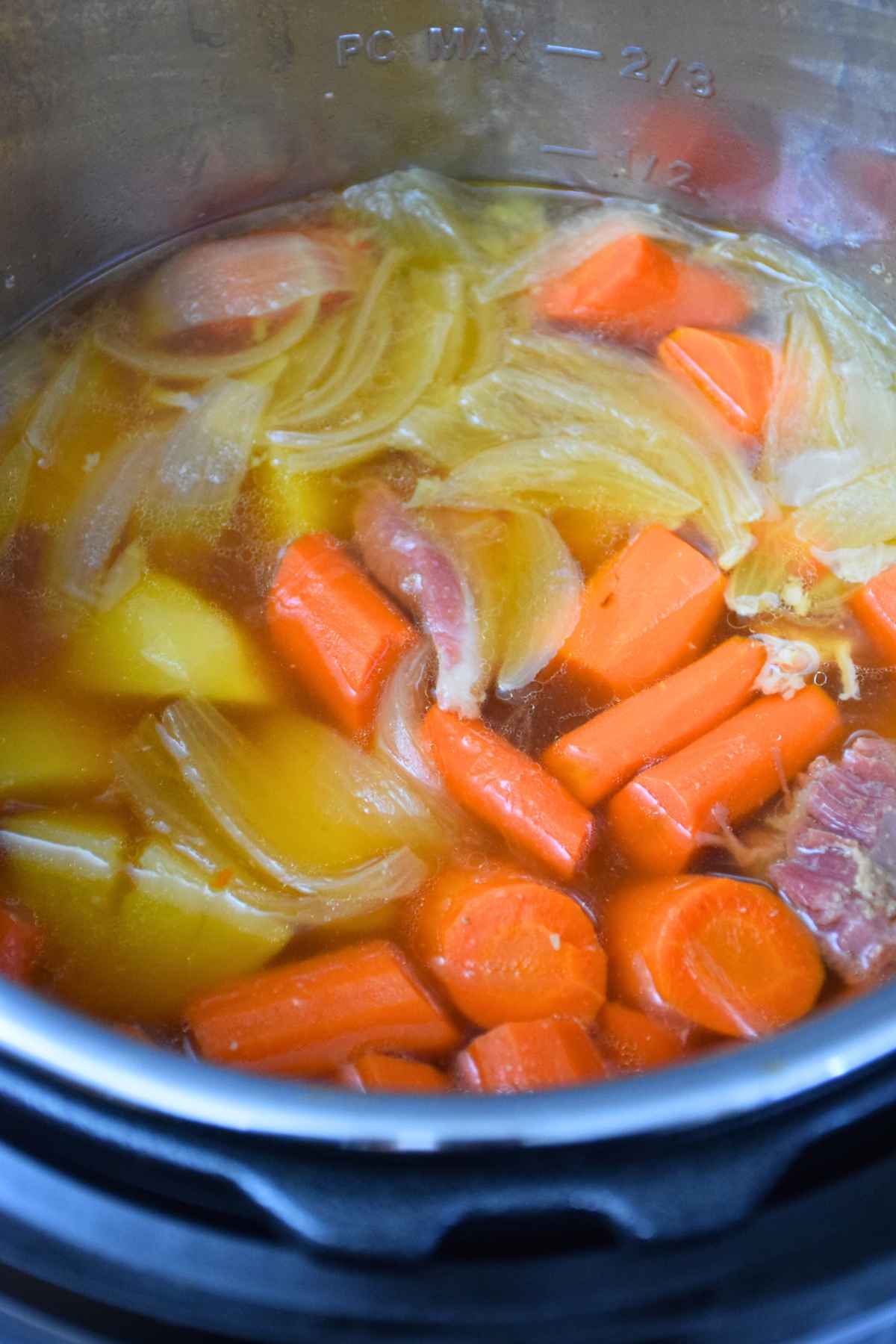 Carrots, potatoes, onions, and ham simmering in broth in an instant pot.