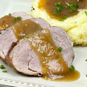 Slices of juicy Instant Pot pork tenderloin topped with savory gravy, served alongside mashed potatoes with gravy and chives.