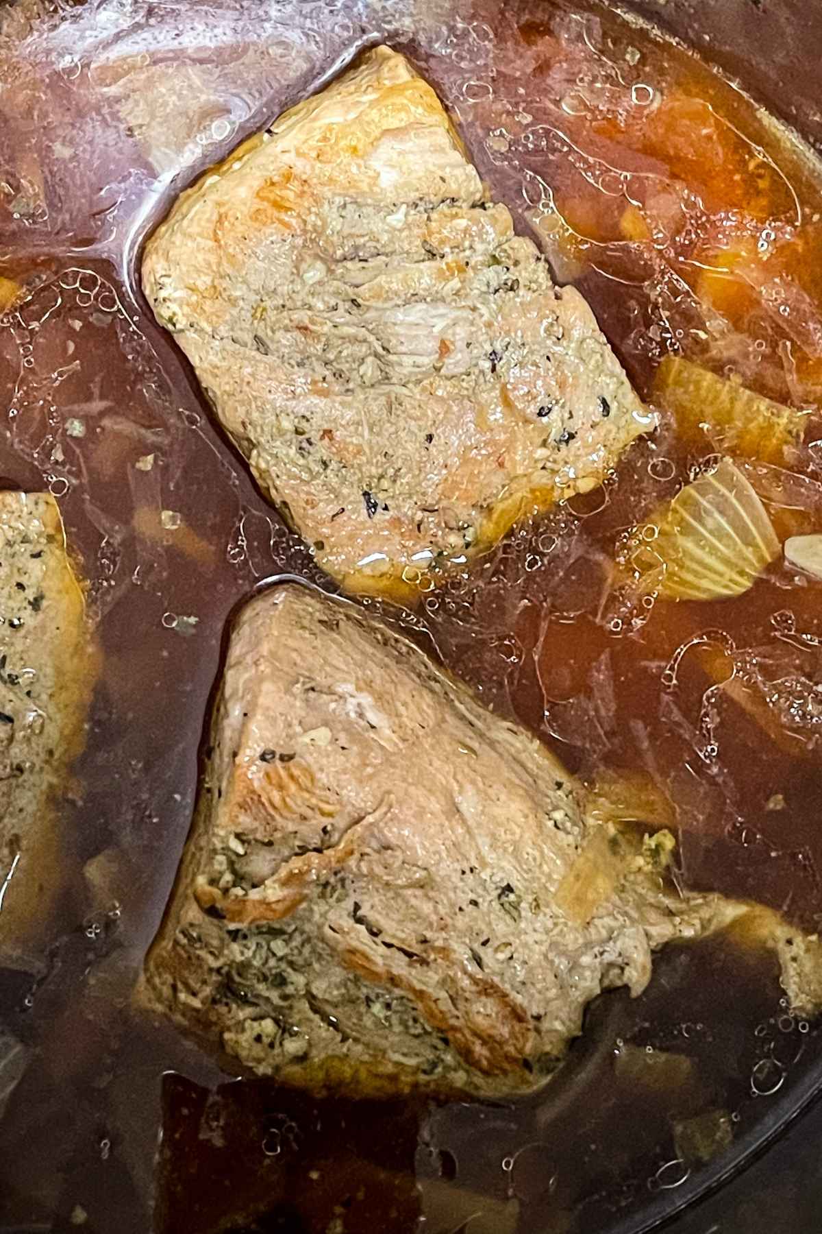Pork tenderloin cooked in an instant pot with broth adn onions, showing tender meat in flavorful liquid.