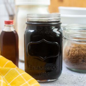 Glass quart jar filled with homemade pancake syrup surrounded by baking ingredients and a yellow cloth.
