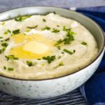 A bowl of creamy mashed cauliflower topped with melted butter and garnished with chopped fresh herbs.