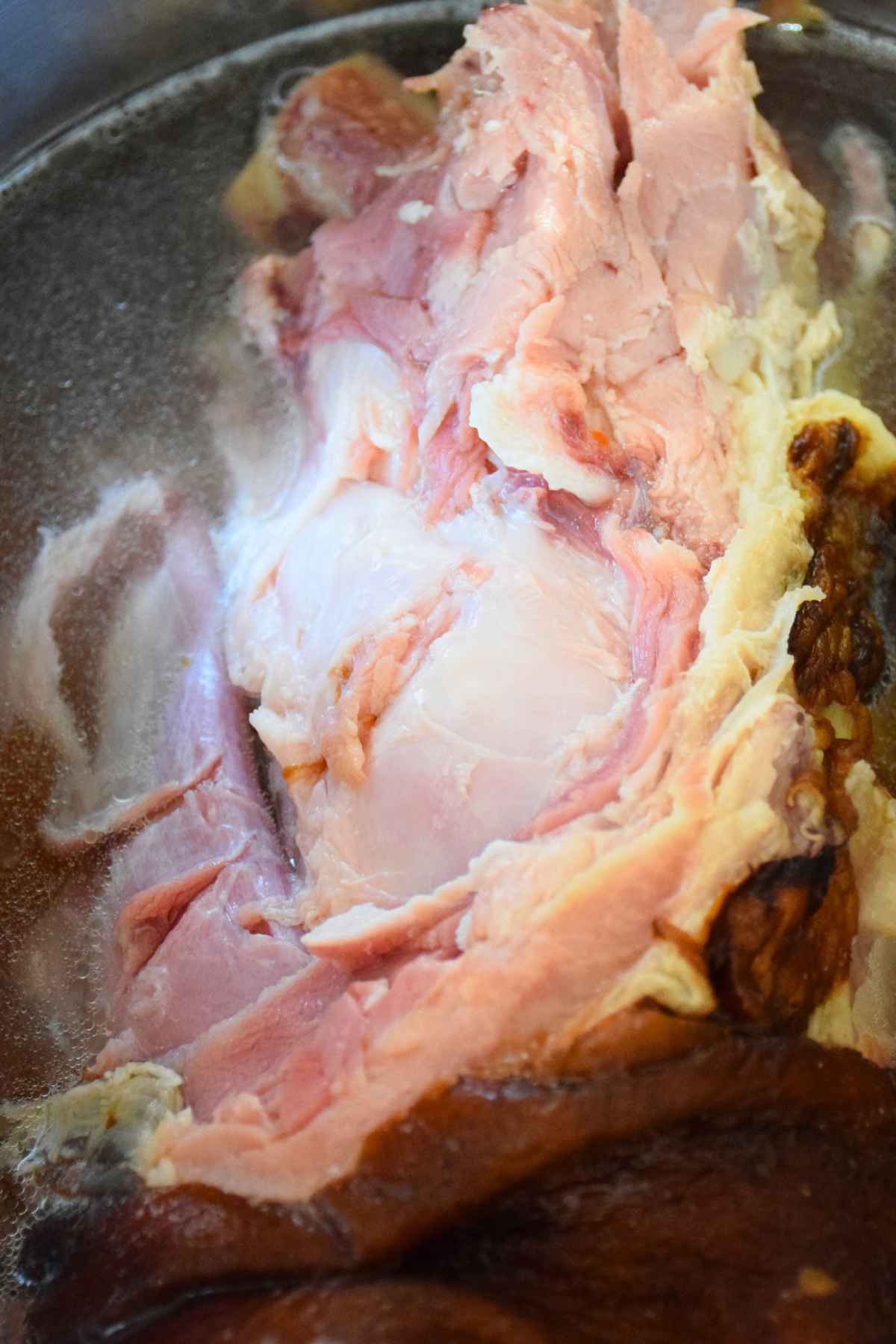 Cooked meaty ham bone in broth inside a pot.