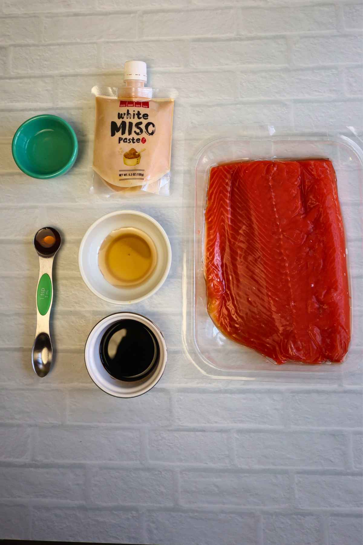 Ingredients for salmon recipe including fresh salmon, miso paste, soy sauce, maple syrup, and rice vinegar.