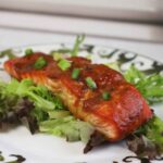 Side view of miso maple salmon served on mixed greens and garnished with scallions.