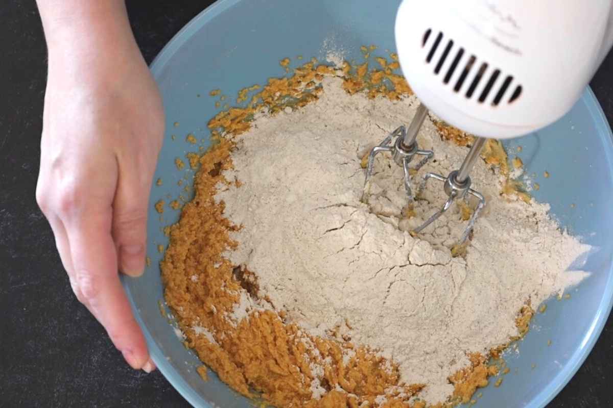 Hand mixer blending flours into a bowl of pumpkin cookie dough.