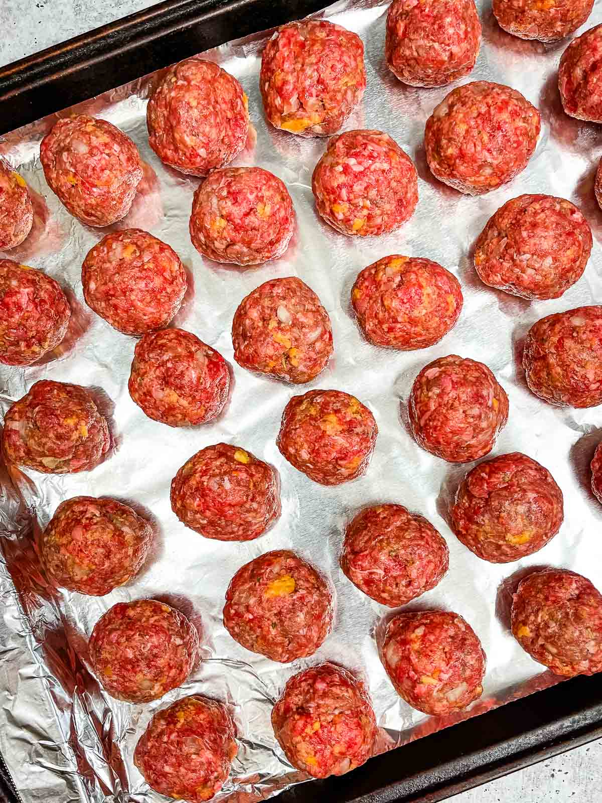 Uncooked meatballs rolled and arranged on a foil lined baking sheet before going into the oven.