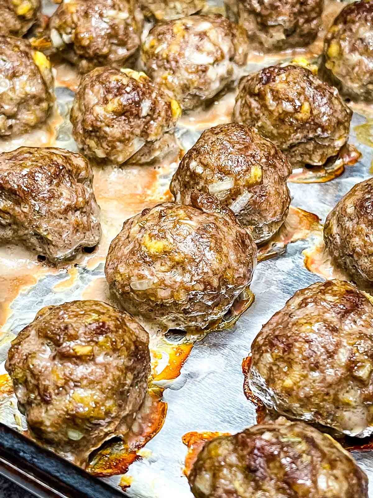 Golden brown oven baked meatballs fresh out of the oven on a foil lined baking sheet.