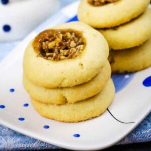 Stack of baked pecan pie thumbprint cookies on a white plate with blue dots.