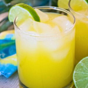 Glass of pineapple agua fresca over ice garnished with a lime wedge.