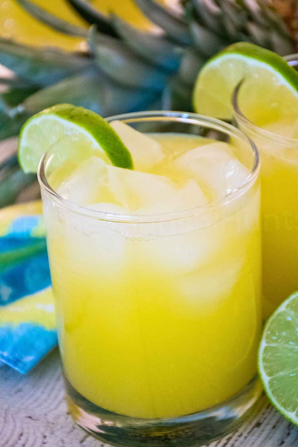 Two glasses of pineapple agua fresca over ice garnished with a lime wedge.