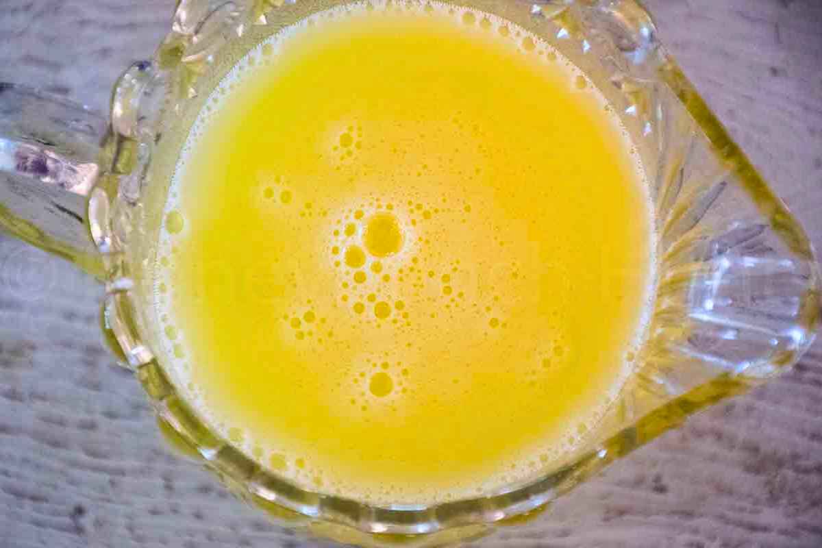 Overhead view of a glass pitcher filled with frothy yellow juice.