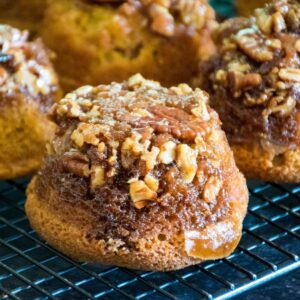 Pecan praline pumpkin muffin topped with chopped pecans and brown sugar glaze, cooling on a wire rack.