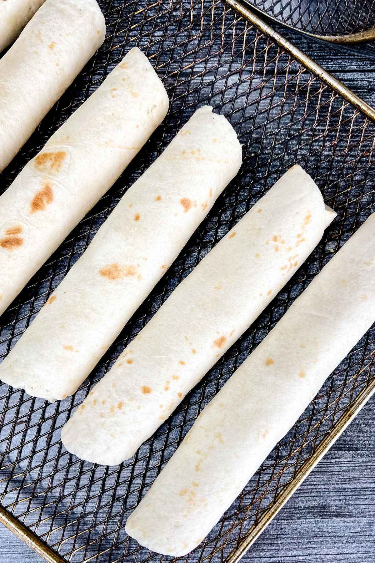 Uncooked taquitos placed on an air fryer tray before cooking.