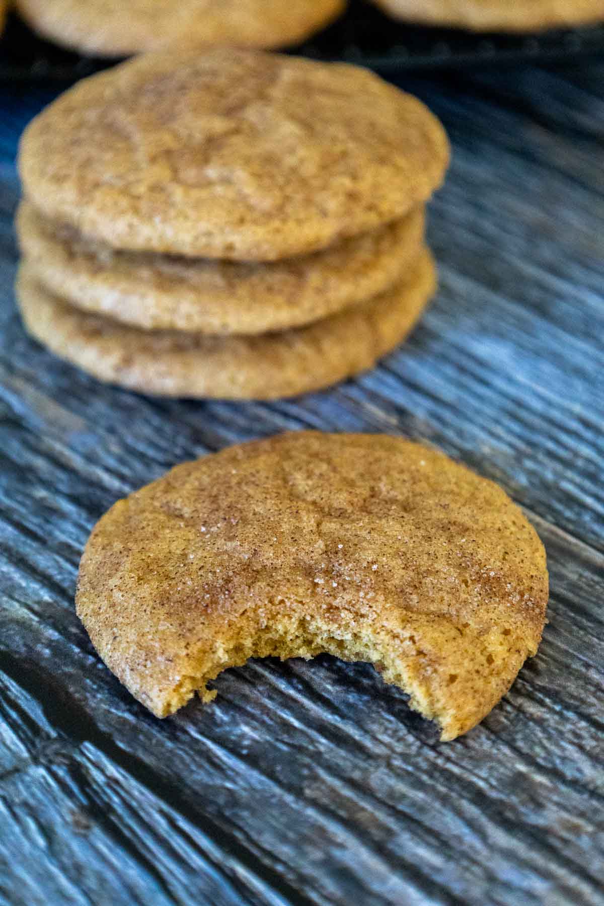 Pumpkin snickerdoodle cookie with a bite taken out, revealing a soft interior, with a stack of cookies in the background.