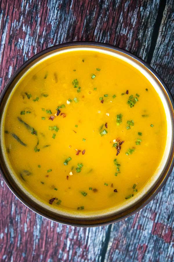 Overhead view of a bowl of creamy pumpkin soup garnished with chopped chives and red pepper flakes.