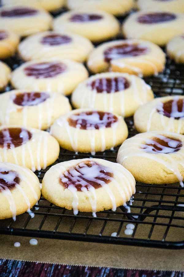 Freshly baked raspberry thumbprint cookies on a cooling rack, drzzled with white icing.