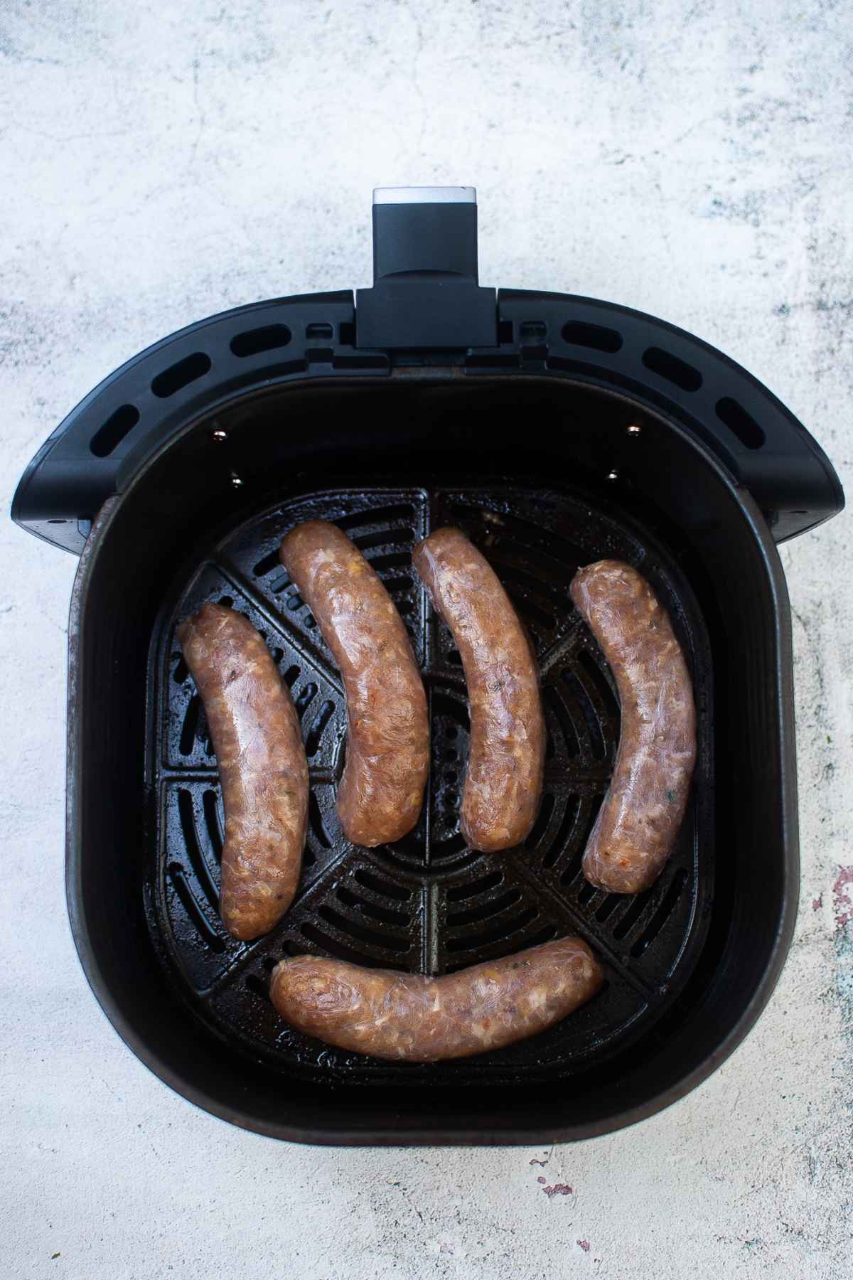 Raw sausage links arranged in an air fryer basket.