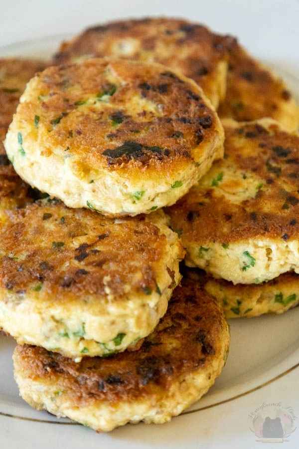 Crispy golden salmon patties stacked on a gold rimmed plate speckled with fresh herbs.