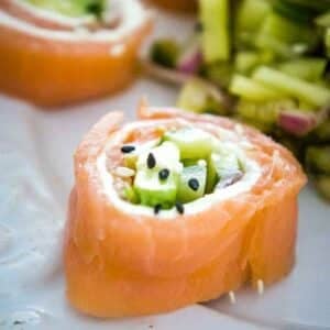 Close up of Salmon Sushi Roll with avocado, cucumber, cream cheese, and black and white sesame seeds served with a cucumber salad on the side.