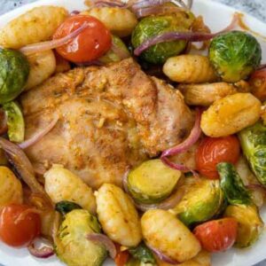 Overhead image of Sheet Pan Chicken and Gnocchi served with golden gnocchi, brussels sprouts, cherry tomatoes, and red onions on a plate.