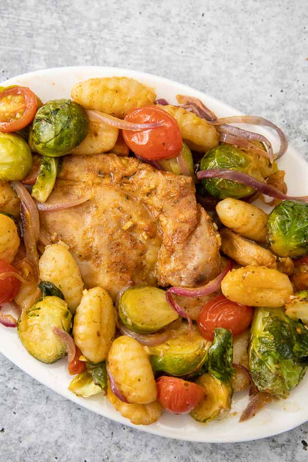 Overhead image of Sheet Pan Chicken and Gnocchi served with golden gnocchi, brussels sprouts, cherry tomatoes, and red onions on a plate.