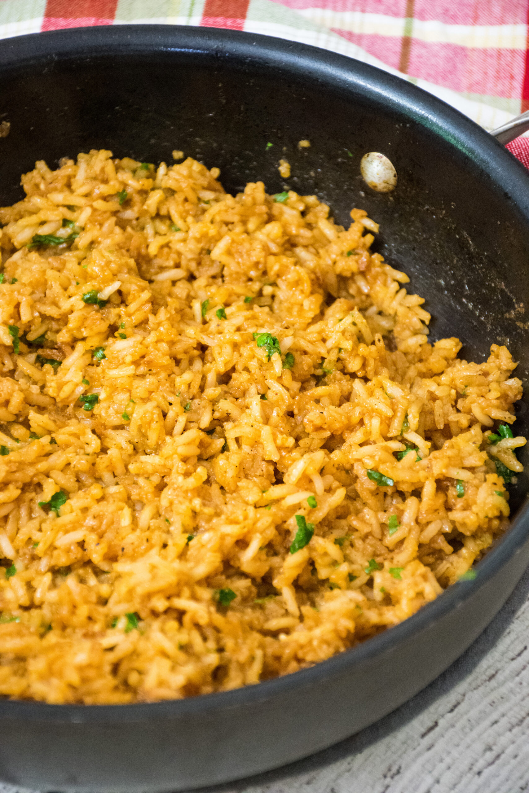 A skillet filled with red rice garnished with fresh cilantro with a red and green plaid towel in the background.